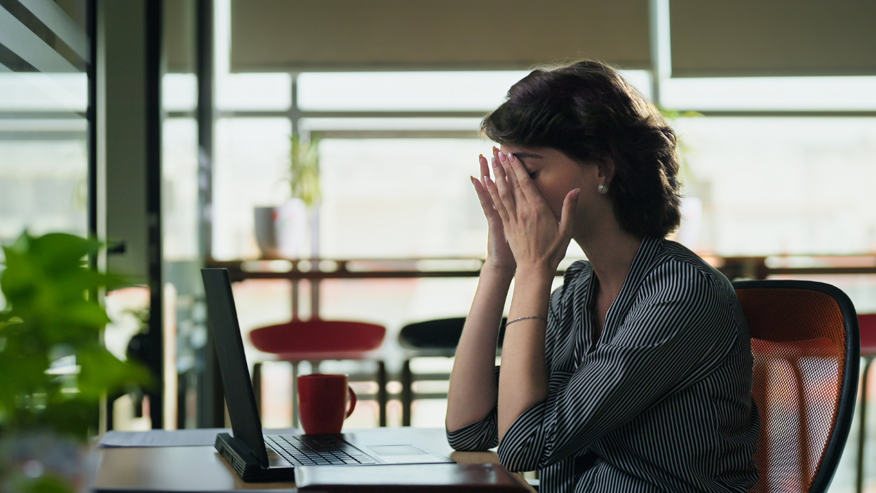 Woman at desk puts face in hands.